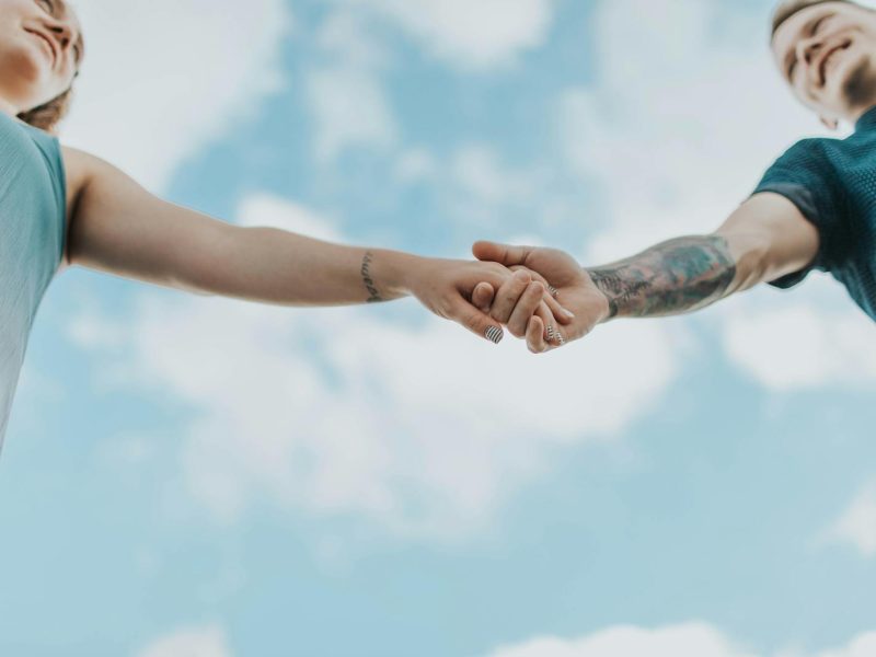 A couple holds hands outdoors, symbolizing love and connection, photographed from a low angle.